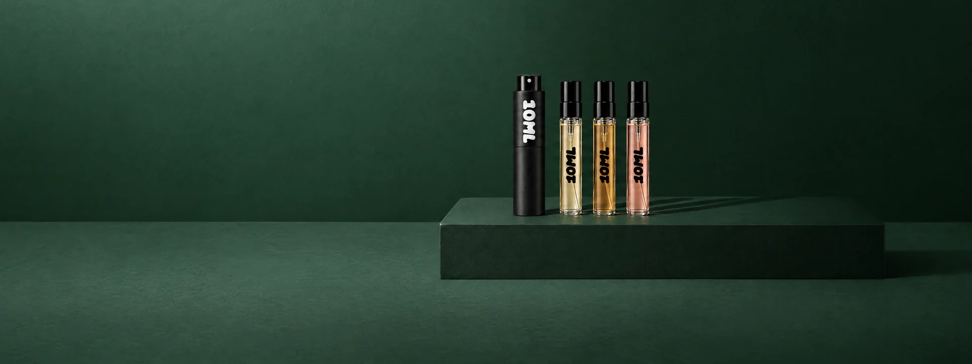 A 10ML atomiser beside three filled sample vials on a dark green plinth