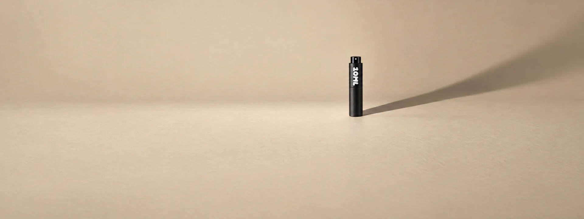 A black 10ML atomiser casting a long shadow on a sand-coloured wall