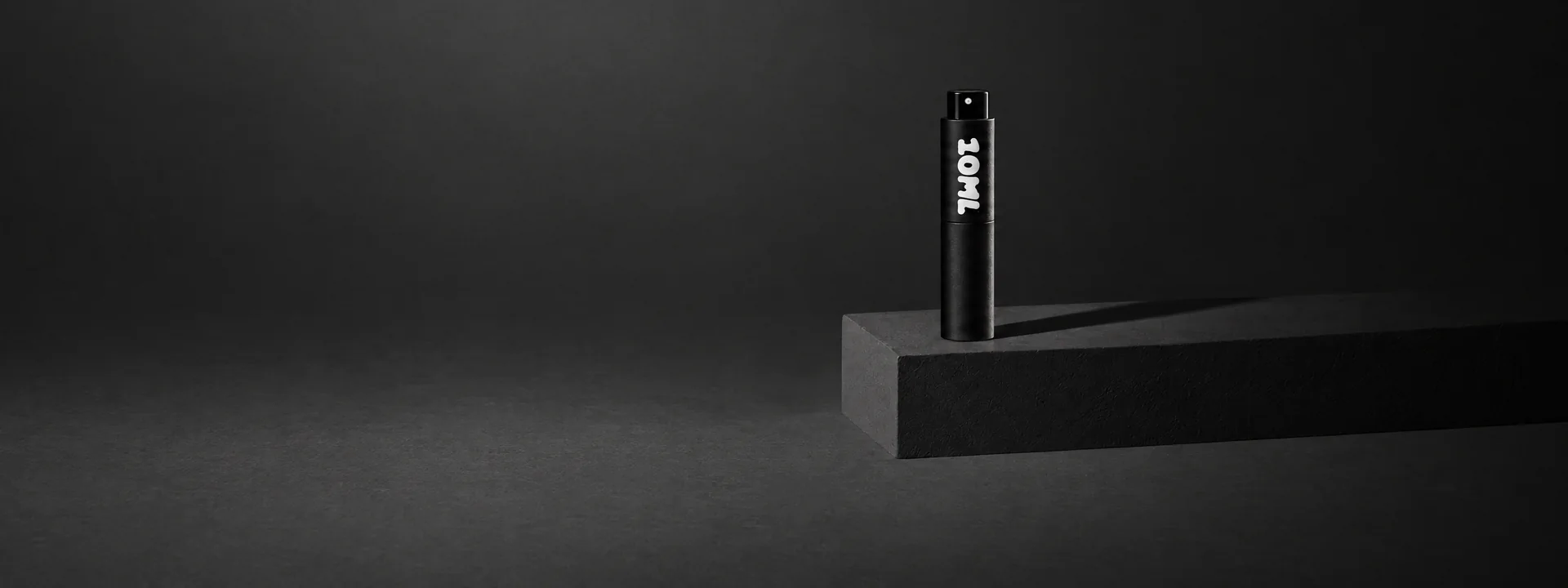 A black 10ML atomiser on a black stone block in low light