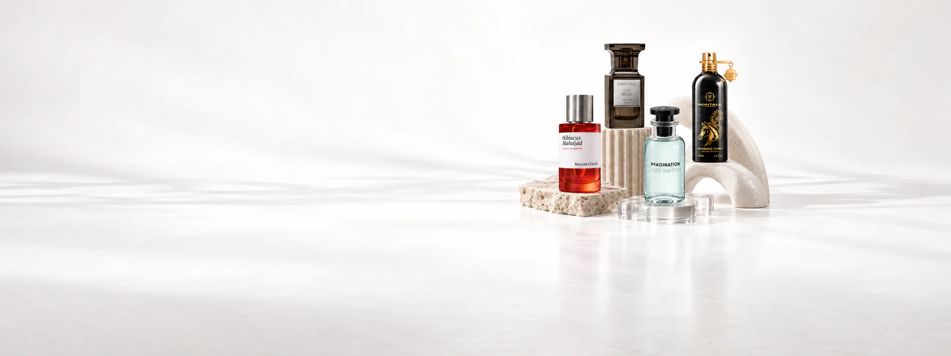 Maison Crivelli Hibiscus Mahajád, Tom Ford Oud Wood, Louis Vuitton Imagination and Montale Arabians Tonka bottles on pale stone