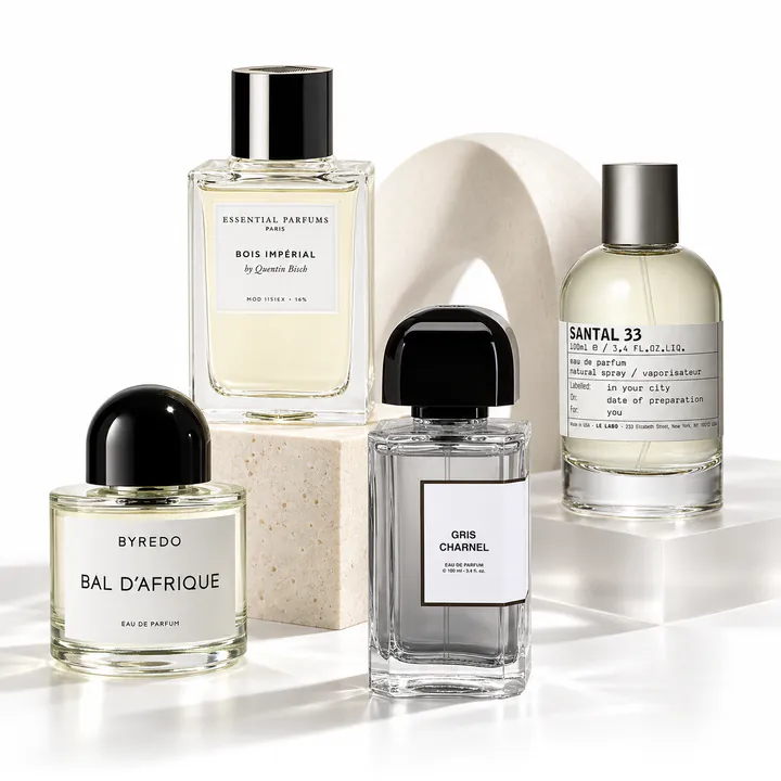 Byredo Bal d’Afrique, Essential Parfums Bois Impérial, BDK Gris Charnel and Le Labo Santal 33 bottles on pale stone