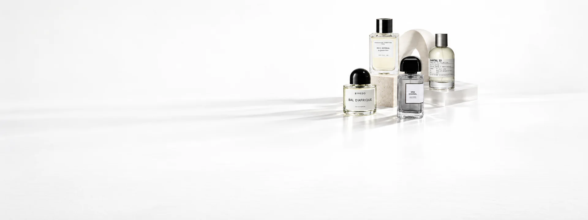 Flacons de Byredo Bal d’Afrique, Essential Parfums Bois Impérial, BDK Gris Charnel et Le Labo Santal 33 sur une pierre claire
