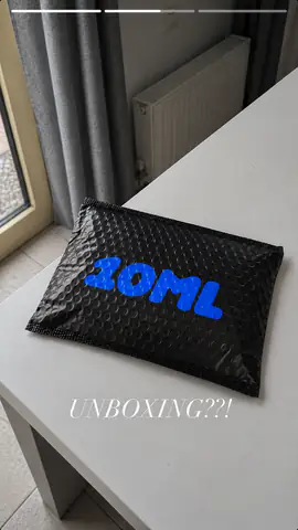 Černá zásilková obálka 10ML na stole s popiskem „Unboxing??!“